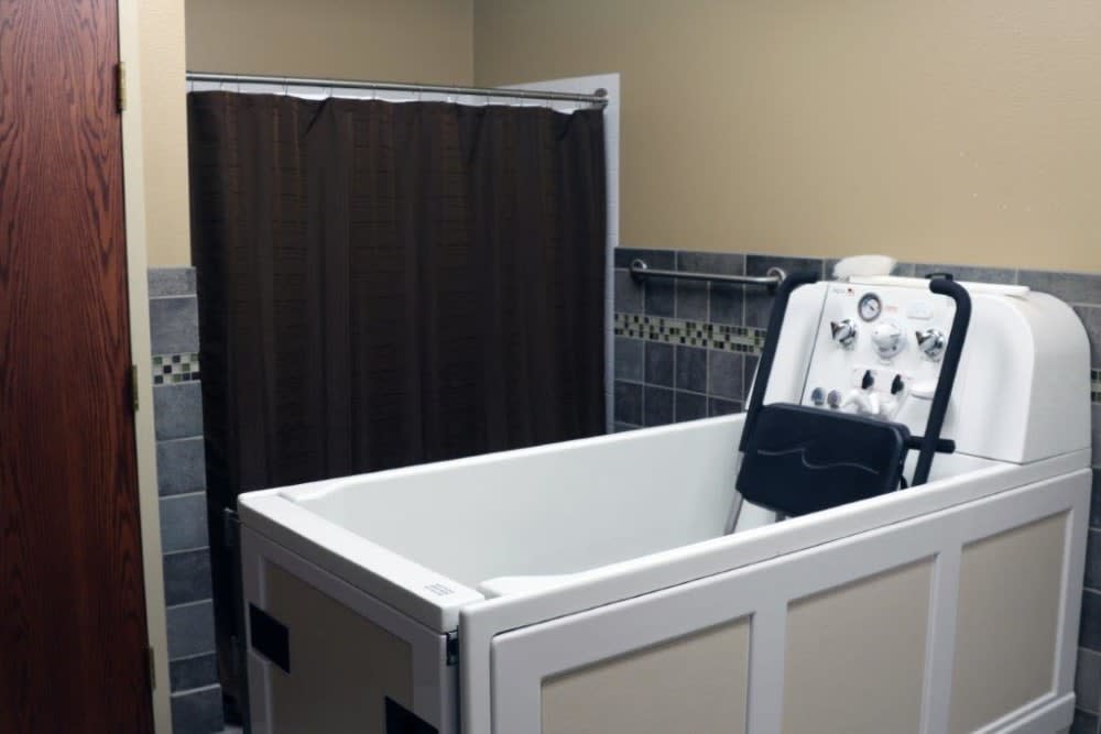 An accessible bathtub with a shower head and curtain in a tiled bathroom.