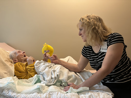A caregiver engages with an elderly individual, providing emotional support and interaction in a warm hospital environment.