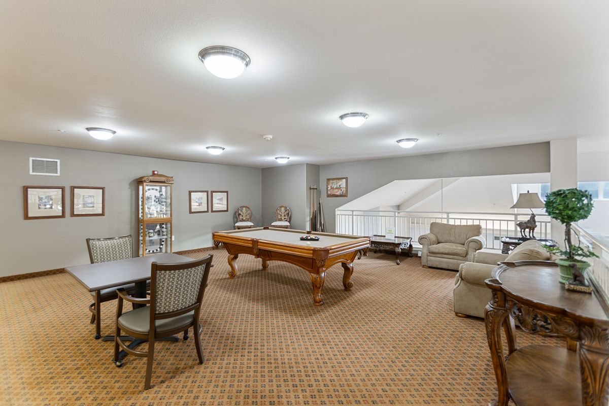 A spacious game room featuring a pool table, seating area, and warm lighting.