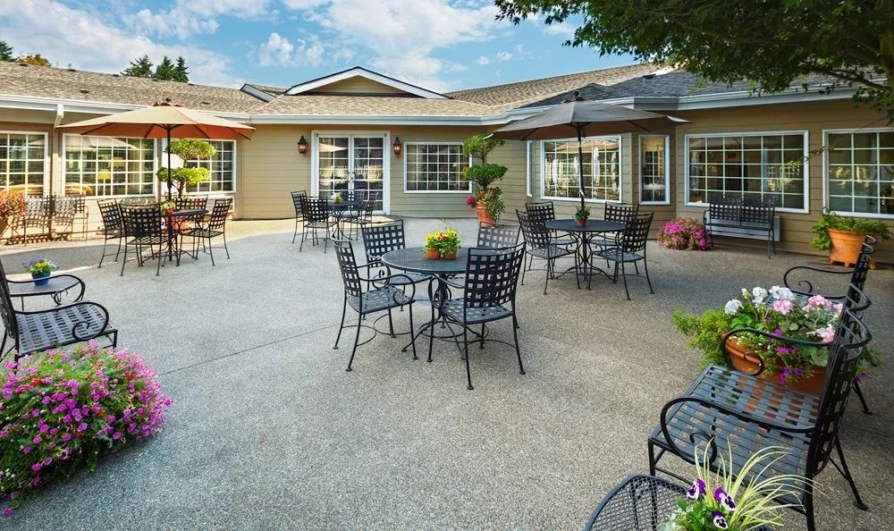 A sunny patio with tables, chairs, and umbrellas outside a residential building.