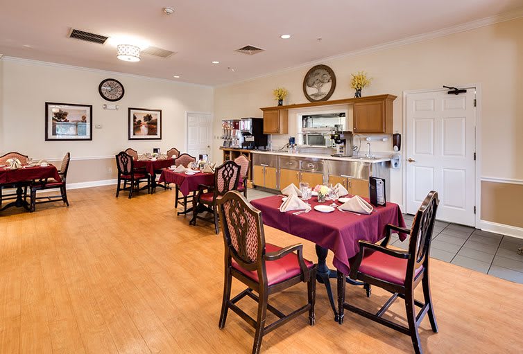 A well-organized dining room with neatly arranged tables and chairs, featuring a kitchen area in the background.