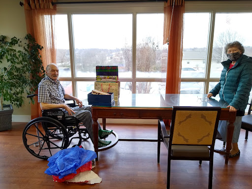 An elderly man sitting in a wheelchair beside a table with a view out the window.