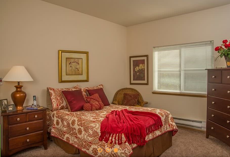 A cozy bedroom with patterned bedding, artwork on the walls, and a window letting in natural light.