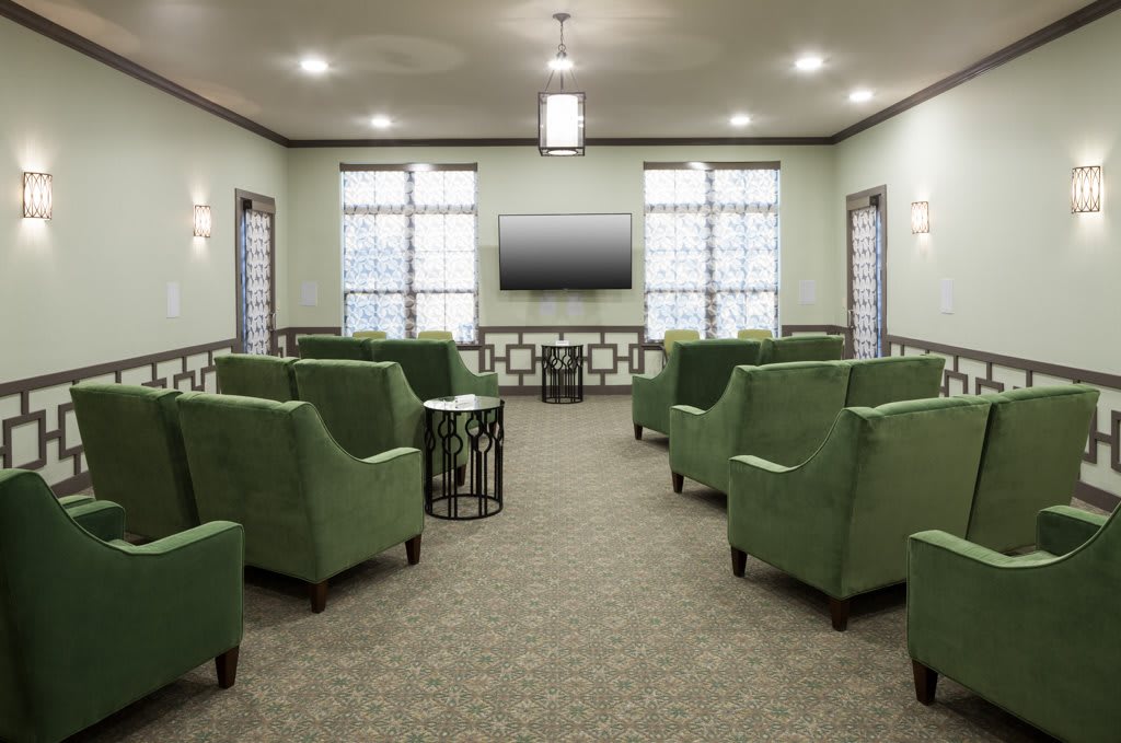A modern lounge with green chairs and a television, featuring large windows and soft lighting.