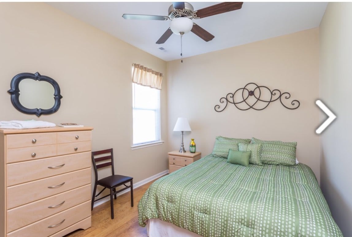 A cozy bedroom with a green bedspread, wooden furniture, and decorative wall art.