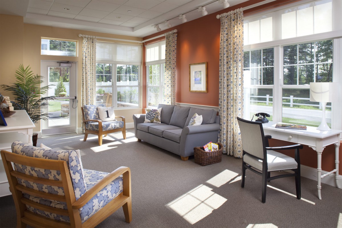 A bright and cozy living room with large windows, a sofa, chairs, and a table.