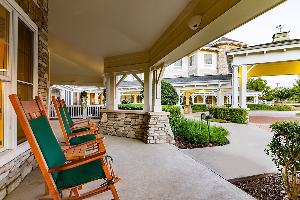 A spacious porch with wooden rocking chairs overlooking a landscaped garden and building.