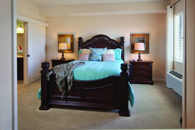 A stylish bedroom featuring a large wooden bed with turquoise bedding, flanked by two bedside tables with lamps.