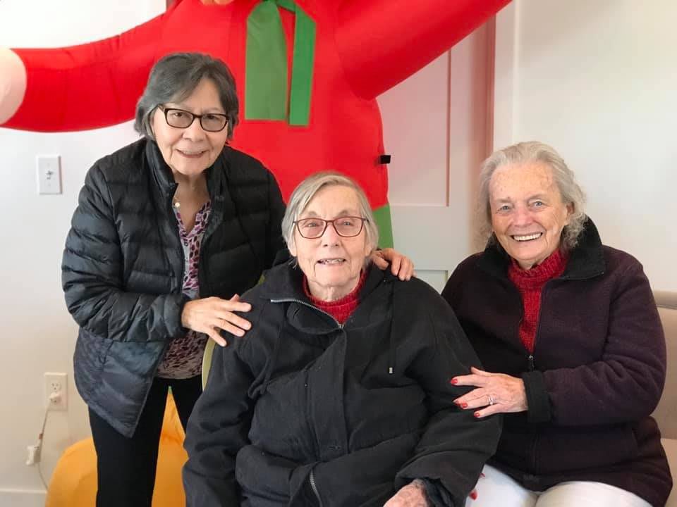 Three elderly individuals smiling together indoors, dressed in winter clothing.