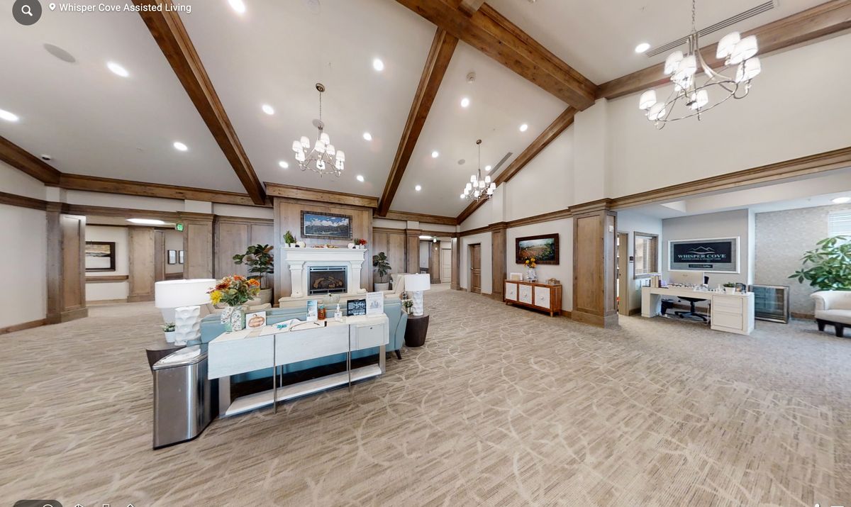 Spacious lobby with chandeliers and wooden ceiling beams, featuring decorative plants and a reception area.