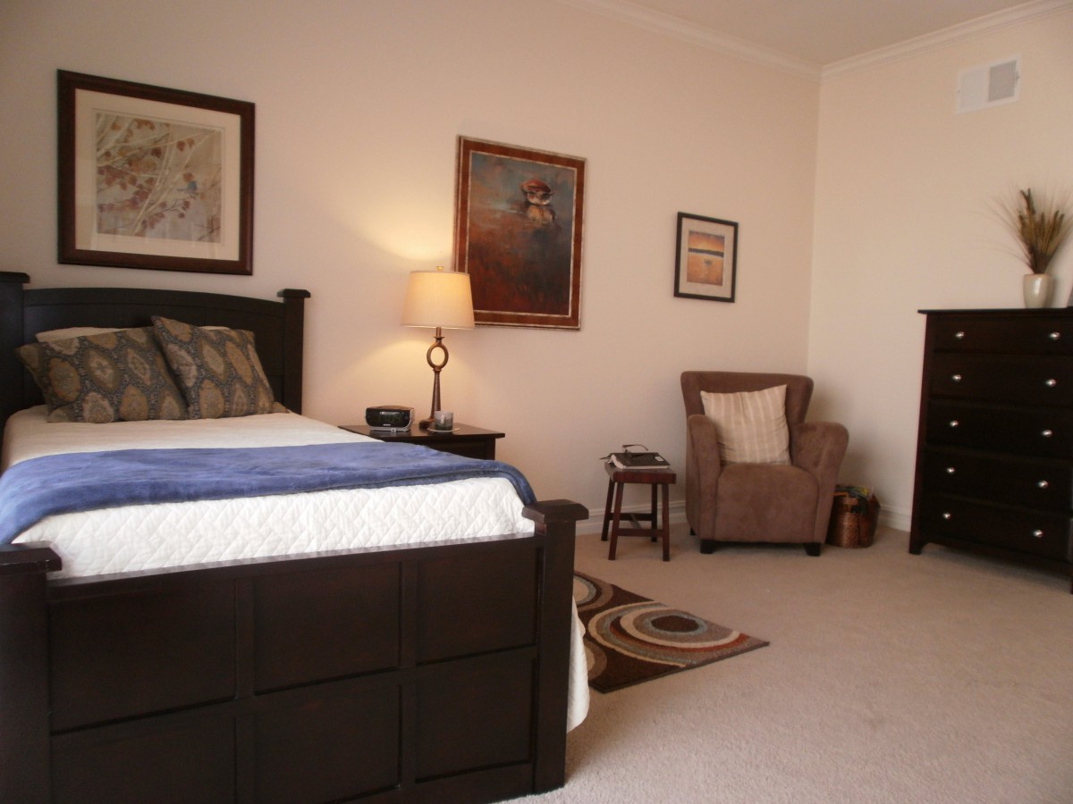 A cozy bedroom with a large bed, armchair, and wall art.