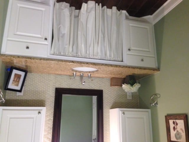 A bathroom interior with a large mirror and cabinets, featuring neatly stacked towels on the shelf.