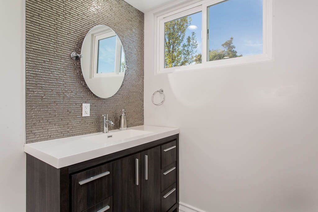 A modern bathroom featuring a circular mirror, sleek vanity, and textured tiled wall.