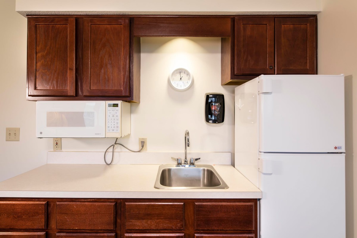 A compact kitchen with wooden cabinets, a sink, microwave, and refrigerator.