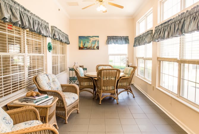 A bright sunroom featuring wicker furniture, abundant natural light, and a cozy dining area with large windows.