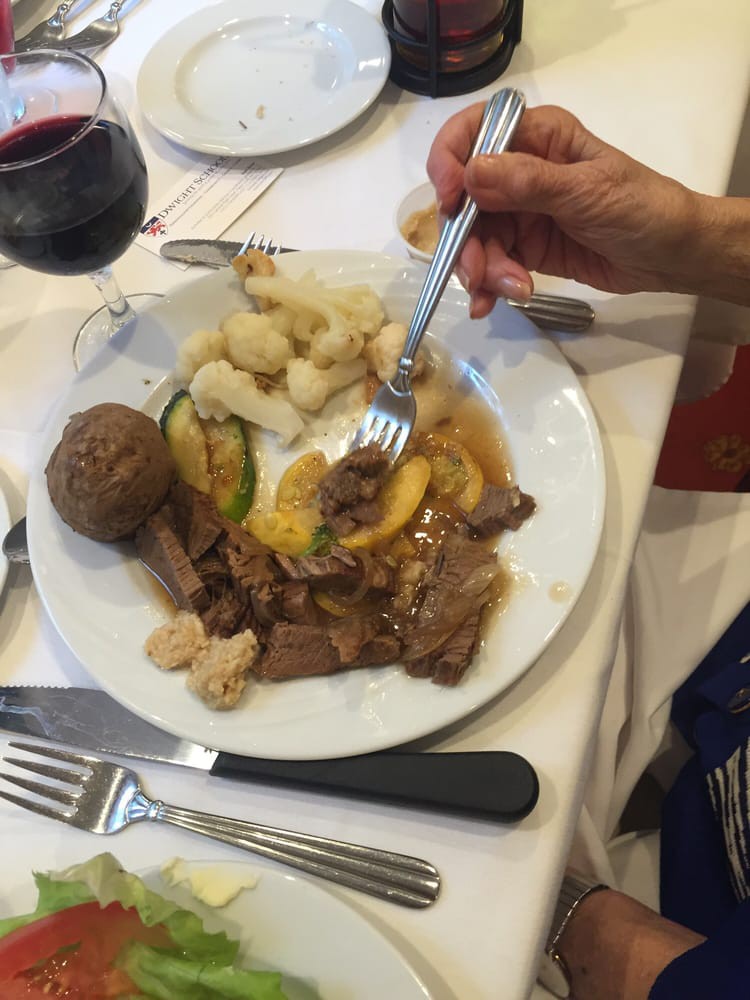 A plate of food featuring beef, vegetables, and a potato with a glass of red wine.