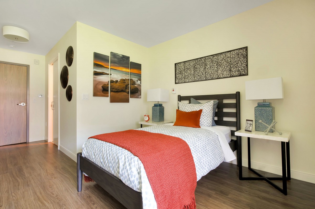 A modern bedroom with stylish decor and artwork, featuring a neatly made bed with vibrant pillows and a throw blanket.