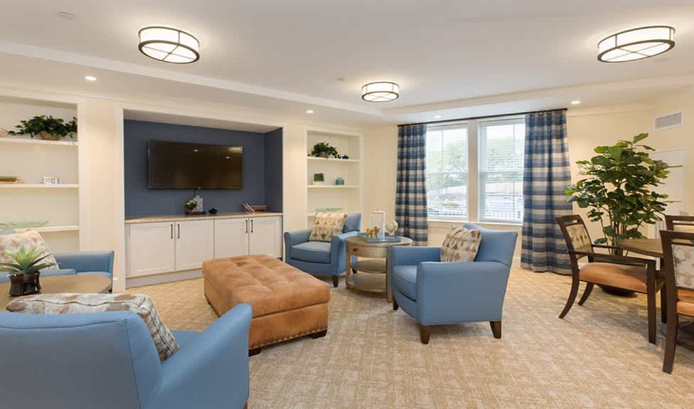 A modern living room with blue chairs, a brown ottoman, and a large television.