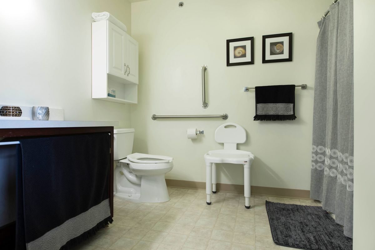 An accessible bathroom featuring a toilet with grab bars and a shower chair.
