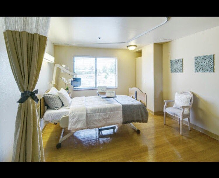 A clean and well-lit hospital room with a bed, chair, and window.