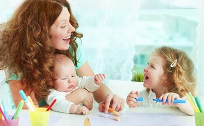 A mother happily interacting with her two children, one a baby and the other a young child.