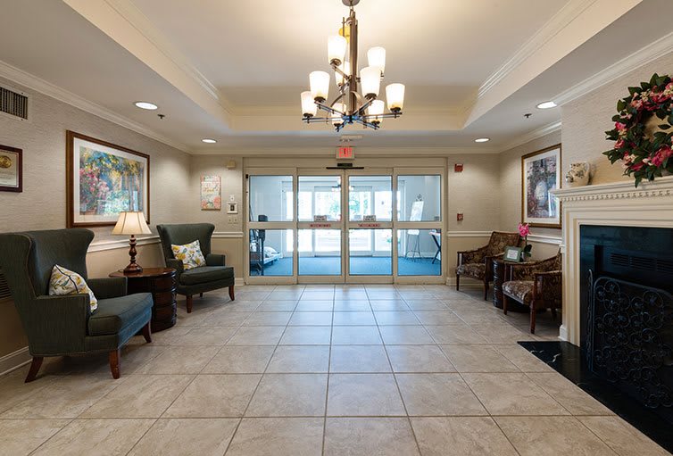 A spacious lobby with a chandelier, seating area, and tiled floor leading to glass double doors.