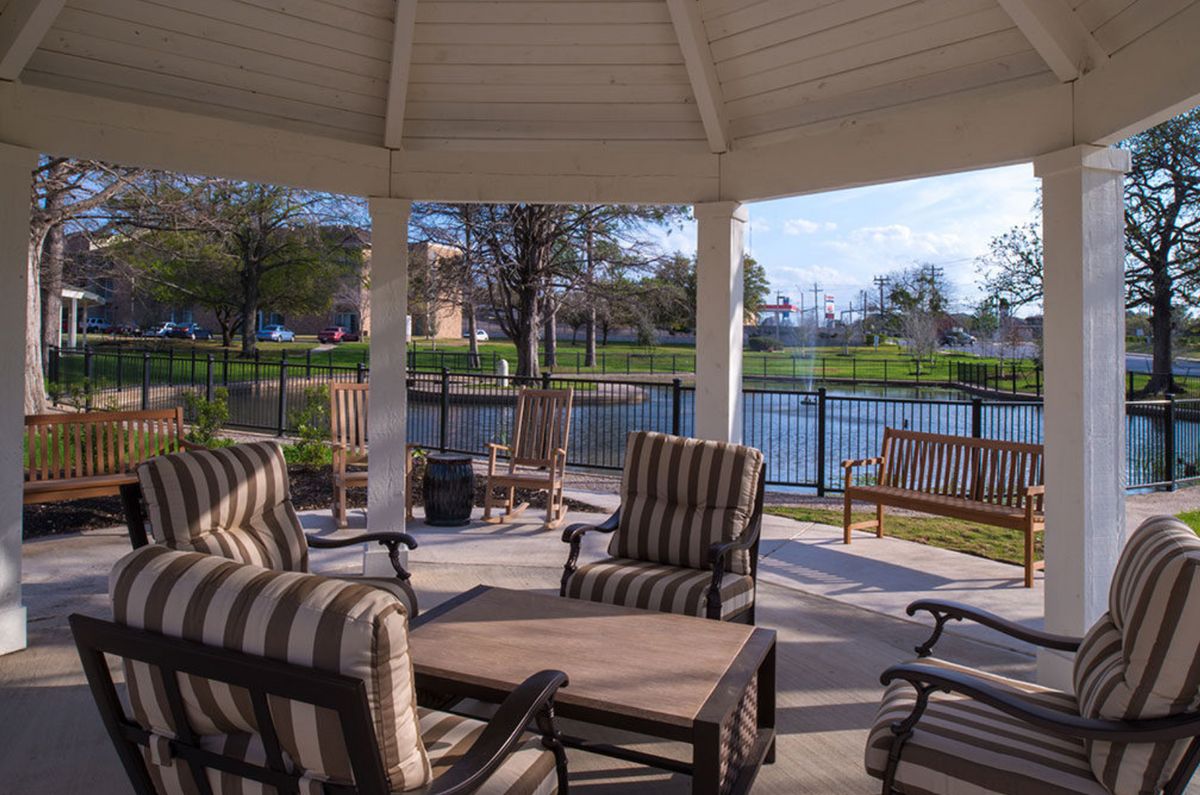 A cozy gazebo with striped patio furniture overlooking a serene lake.