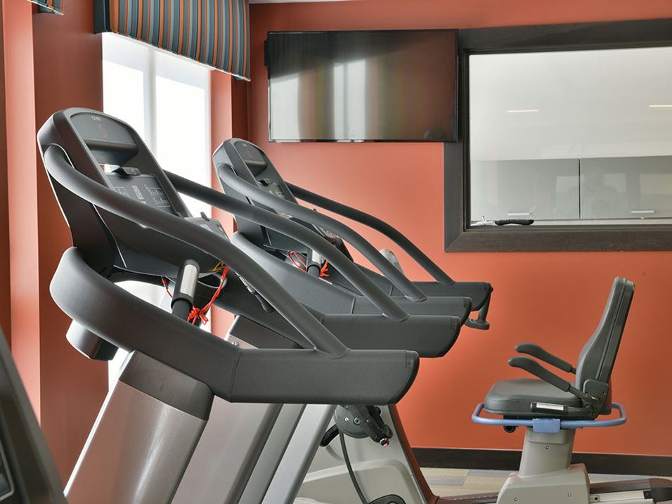 A gym with treadmills lined up against a red wall.