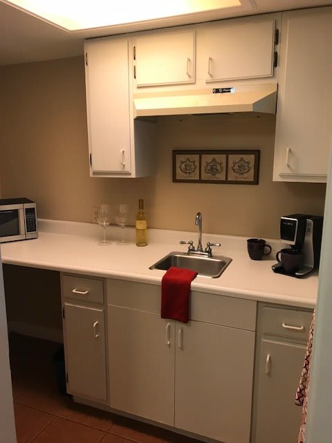 A compact kitchen with a white countertop, featuring a microwave, coffee maker, and decorative wall art.