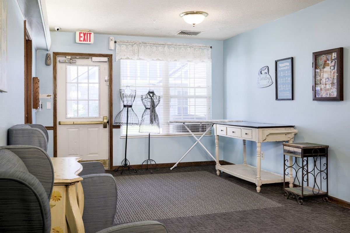 A bright room with light blue walls, featuring a table, chairs, and a large window allowing natural light to illuminate the space.