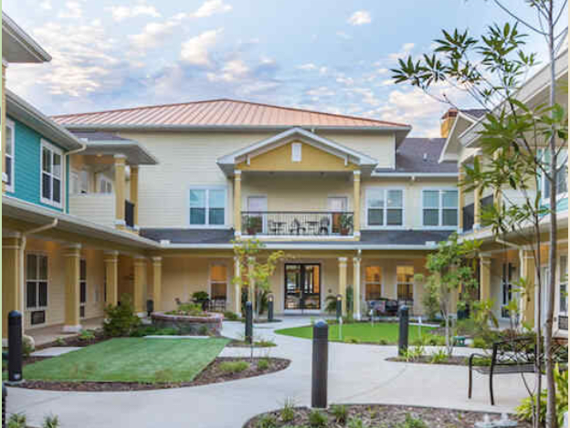 A two-story residential building with a courtyard and landscaped surroundings under a partly cloudy sky.