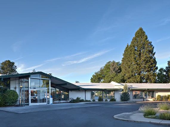 A mid-century modern building with a glass facade surrounded by trees under a clear blue sky.