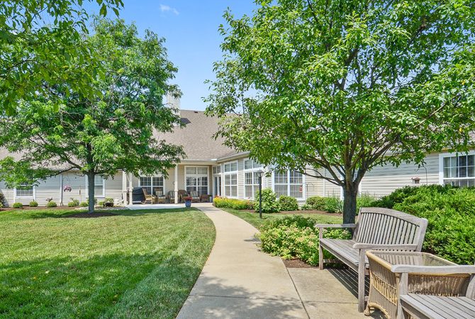A serene garden path leading to a building, surrounded by lush greenery and benches.