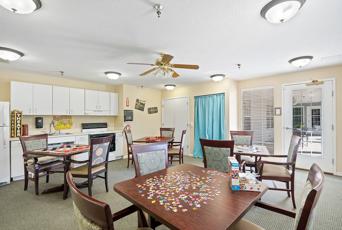 A cozy dining area with tables set up for games and meals, featuring a ceiling fan and a small kitchen area.