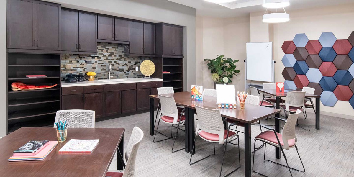 A modern classroom setup with tables, chairs, a whiteboard, and a kitchenette.