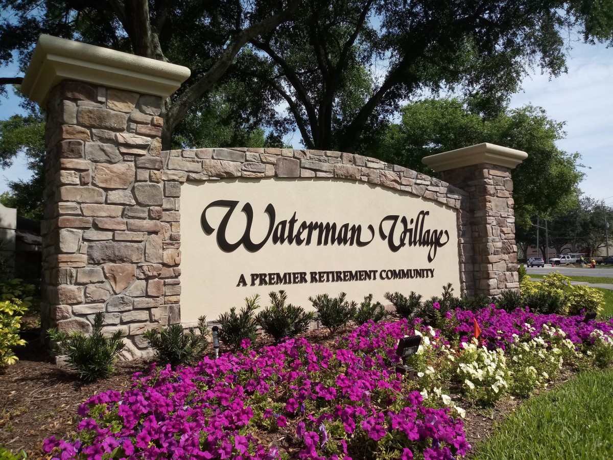 Entrance sign for Waterman Village, a premier retirement community, surrounded by vibrant flowers.