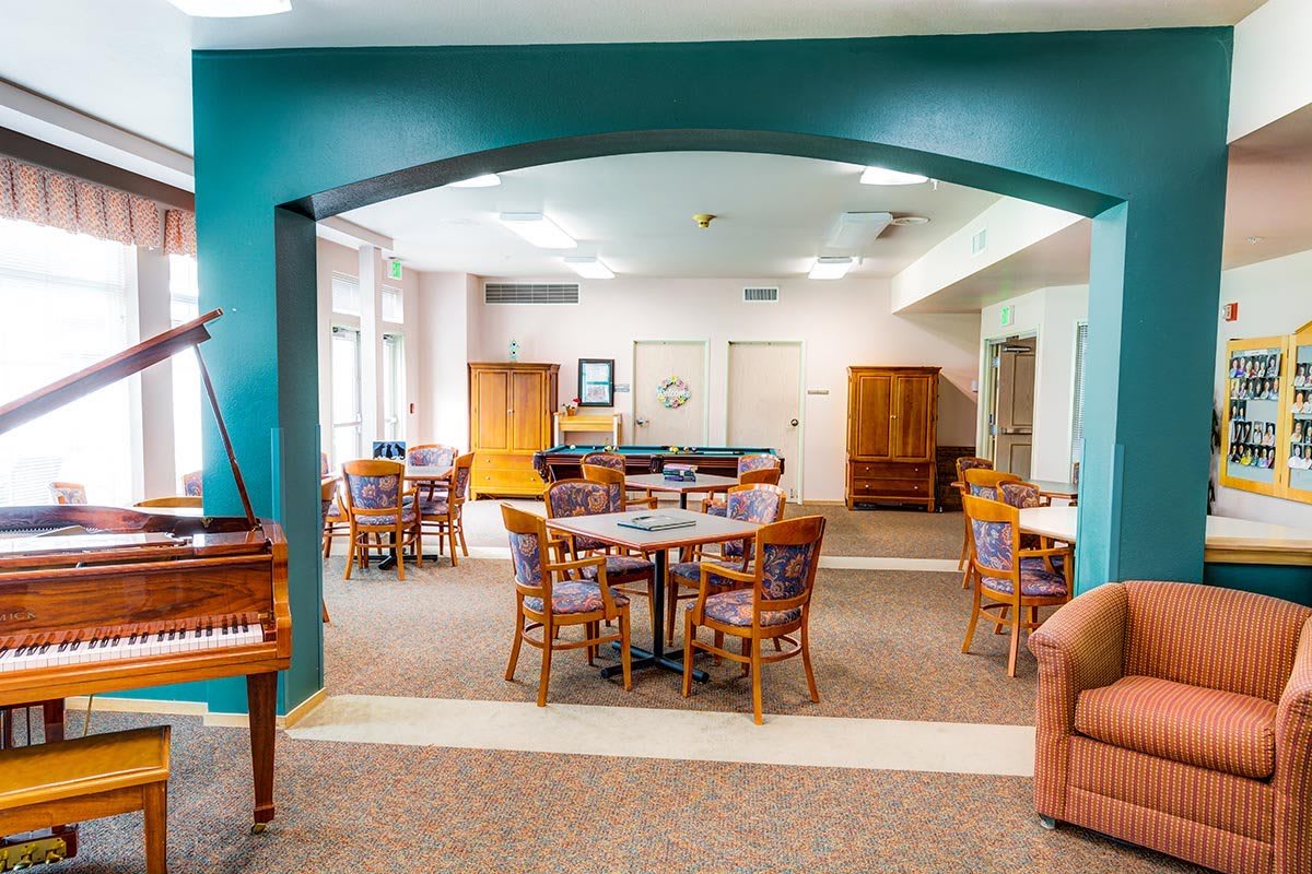 A bright and spacious community dining area with tables, chairs, and a piano.