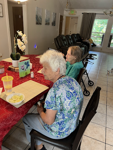 Two elderly women seated at a dining table in a care facility, engaged in conversation.
