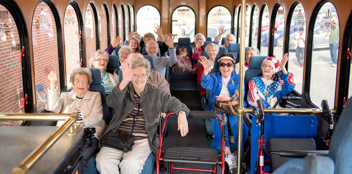 A group of seniors enjoying a bus tour, waving cheerfully.