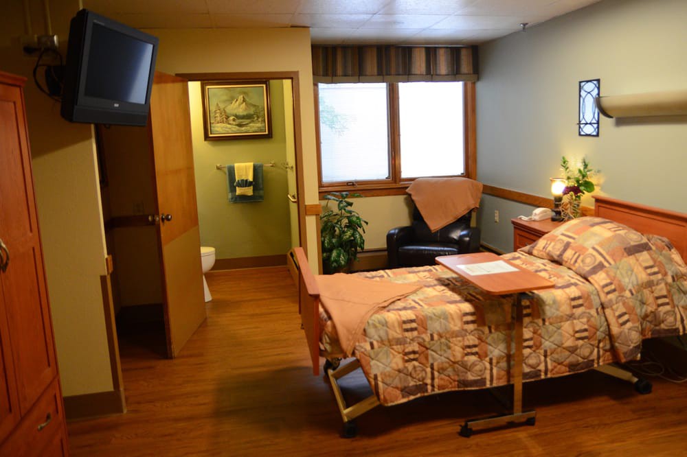 A cozy hospital room with a bed, TV, and large windows providing natural light.