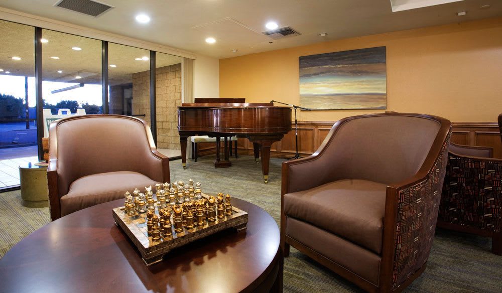 A cozy living room with a grand piano, a chessboard on the table, and comfortable chairs.
