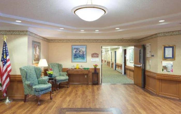 A cozy waiting area with chairs, a table, and a painting on the wall, leading to a hallway.