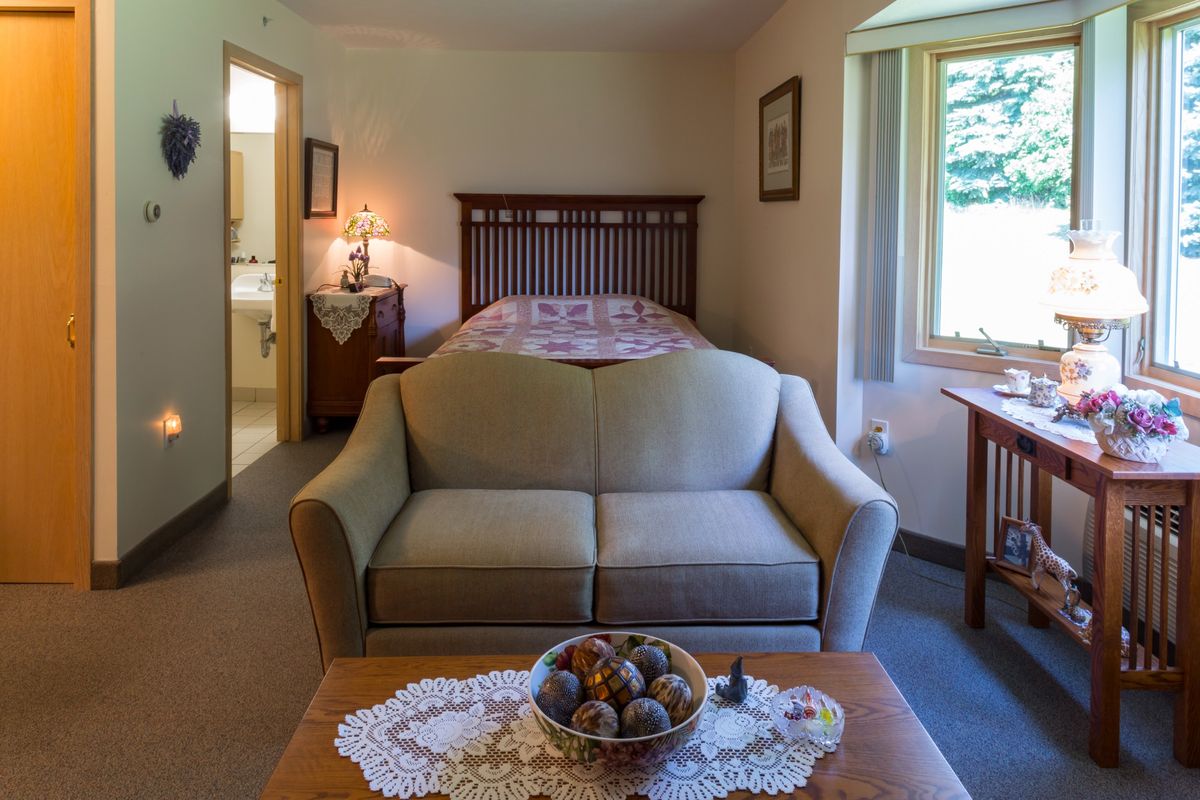 A cozy bedroom with a sofa facing the bed, featuring a window and homey decor.