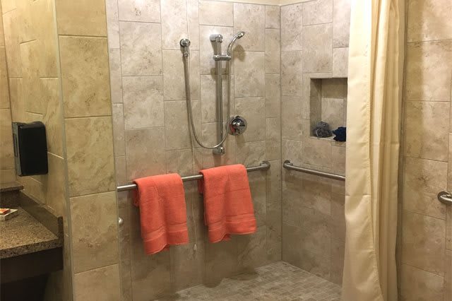 A walk-in shower with tiled walls and orange towels hanging on a bar.