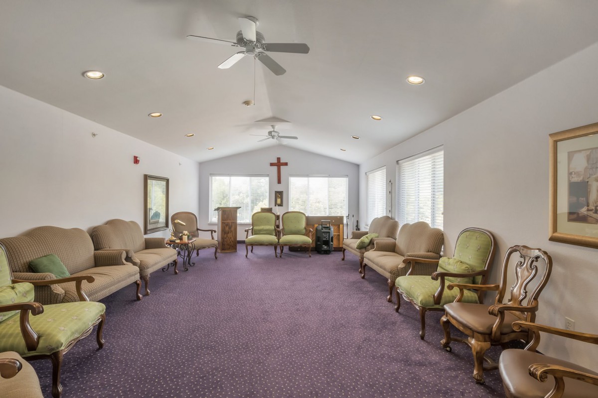 A meeting room with chairs arranged in a circle, featuring ceiling fans and a cross on the wall.