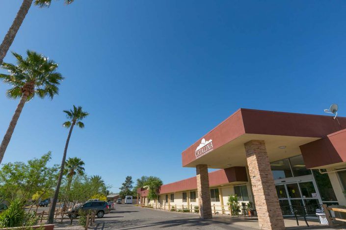 A motel with palm trees and a clear sky, featuring a parking lot in front.