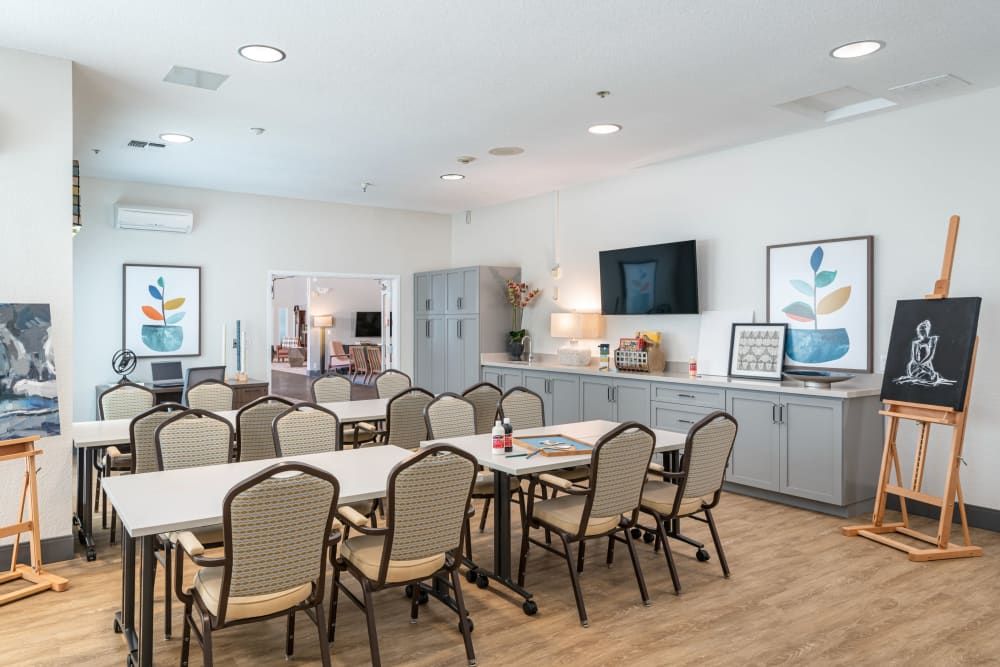 A spacious community room with tables and chairs arranged for meetings, featuring a television and wall decorations.