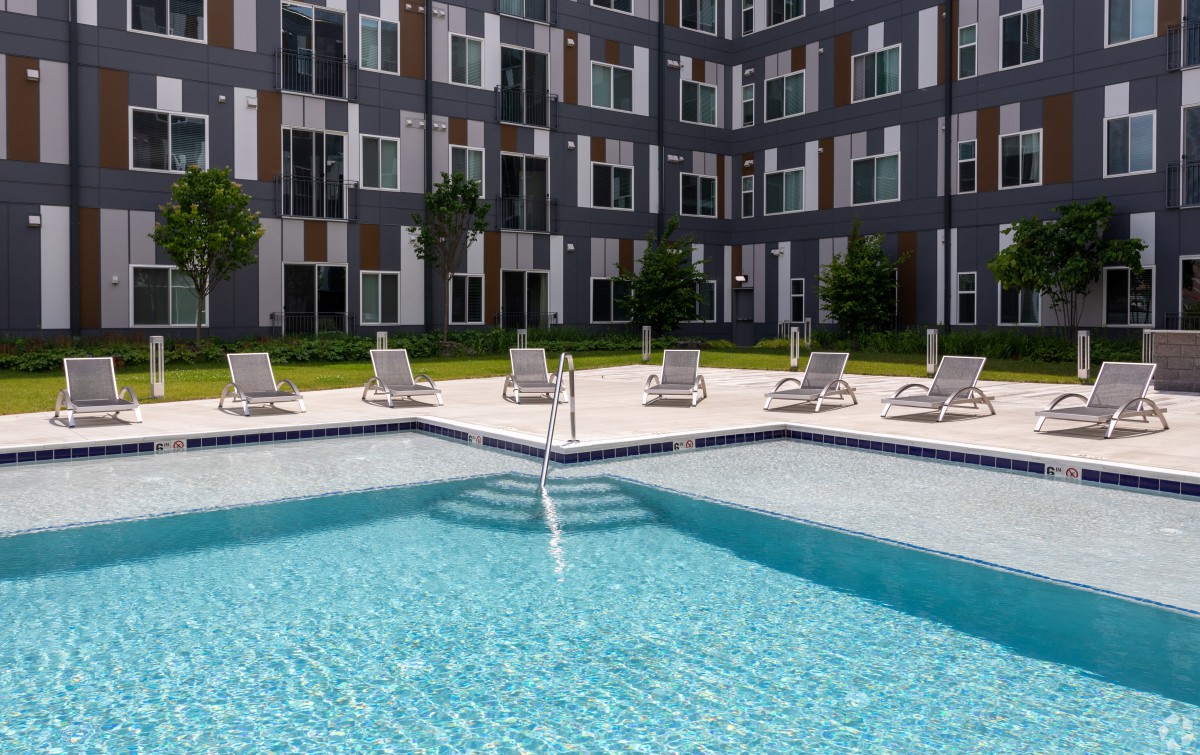A modern apartment complex with an outdoor swimming pool and lounge chairs.