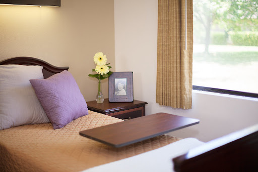 A cozy bedroom setup featuring a neatly made bed, a vase of flowers, and a picture frame on the nightstand.