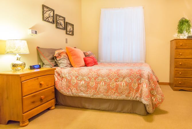 A cozy bedroom with a neatly made bed, colorful pillows, and a wooden dresser.